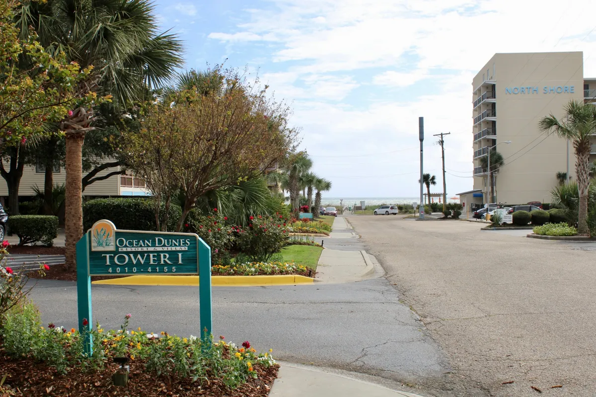 This exterior shot showcases the Ocean Dunes sign, the impressive Tower I, and a beautifully landscaped garden, with hints of the ocean in the background. The image gives a sense of arrival, the property's central location, and its proximity to both the beach and outdoor relaxation areas.