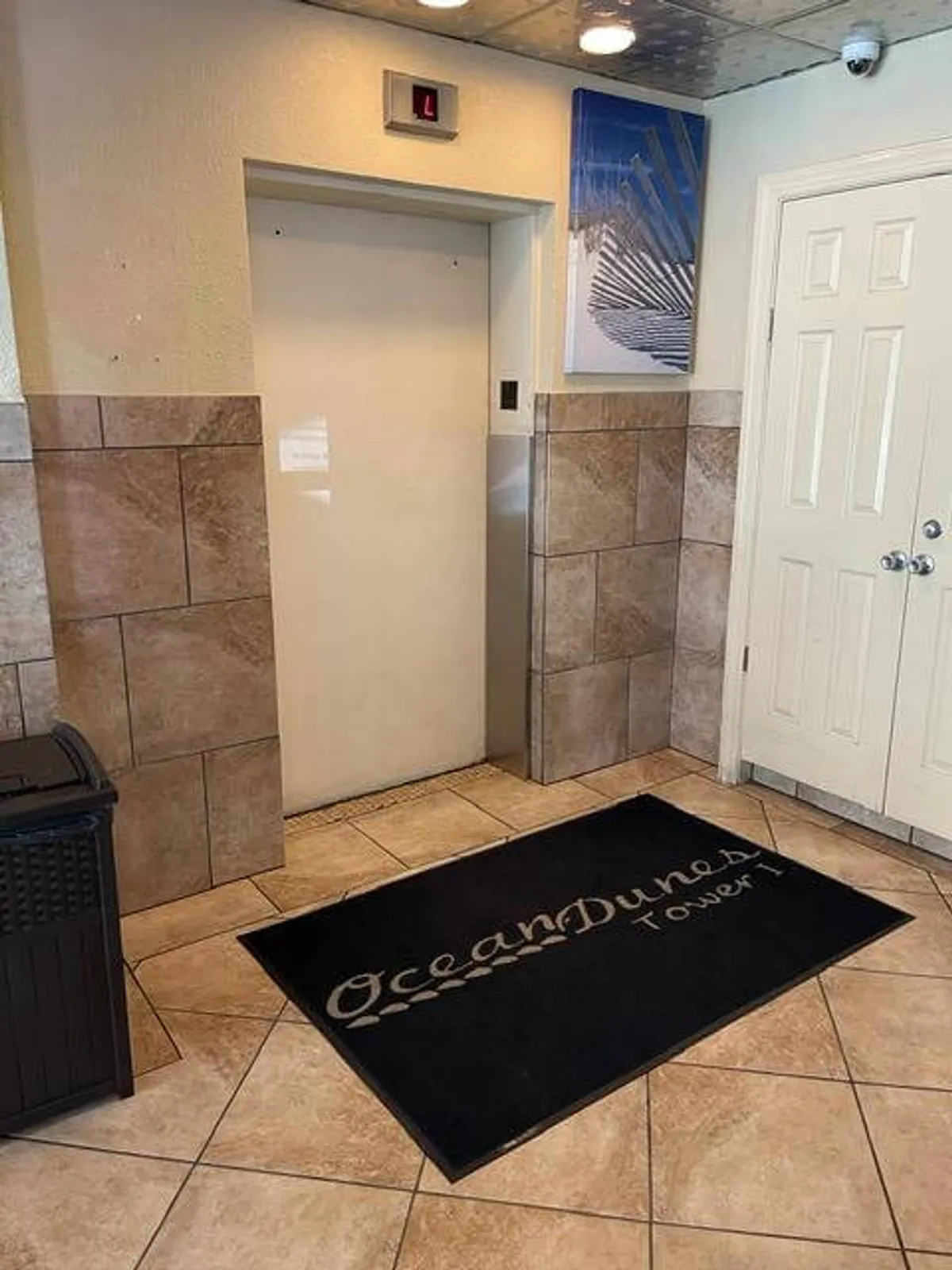 An inviting interior view centering on an elevator lobby with a welcome mat, decorative wall art, and doors leading to residences. The space is bright and suggests easy access to both the condo and resort facilities.