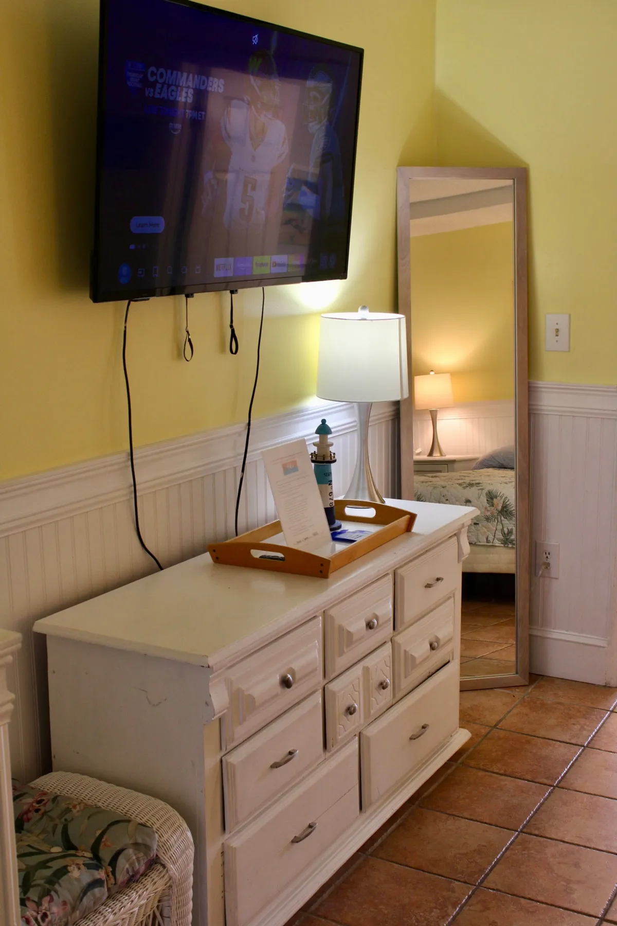 A cozy living room scene with a TV showing sports content, a dresser with decorative items, and comfortable seating, creating an inviting communal space ideal for group gatherings and shared downtime.