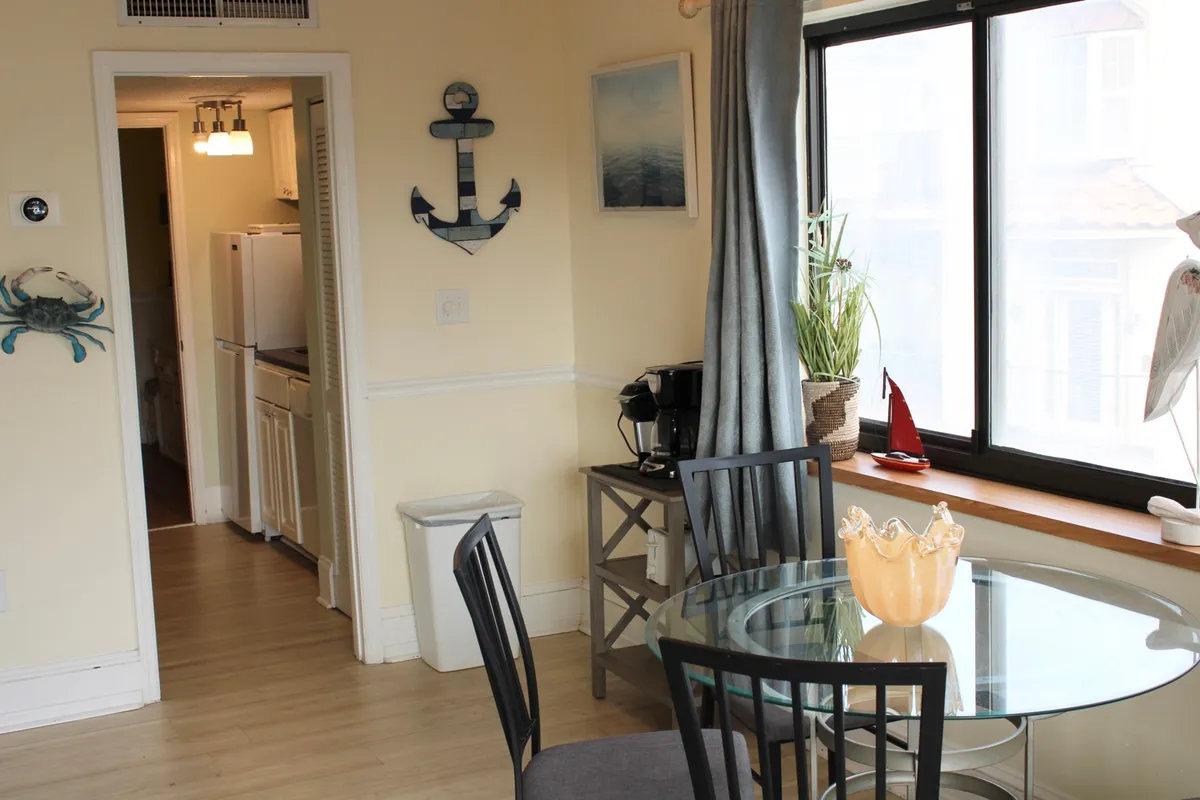 A cozy dining area featuring a dining table set by a window, adorned with a decorative anchor and a potted plant. Natural light creates a relaxed atmosphere, perfect for enjoying casual meals or morning coffee while taking in the view.