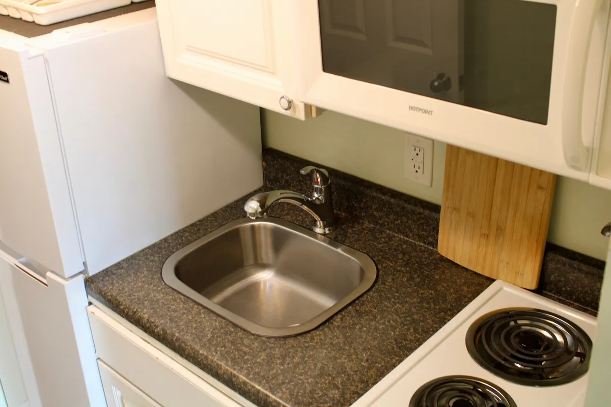 A compact, well-equipped kitchenette featuring a sink, stove, microwave, and a cutting board on the countertop. The setup exudes a practical yet inviting atmosphere, emphasizing the space's readiness for cooking and meal preparation.